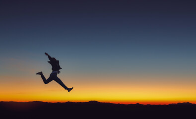 Silhouette of beautiful girl jumping on mountain park golden color sunset background.