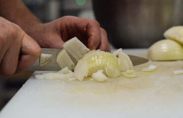Restaurant kitchen employee cutting onions with knife closeup