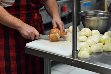 Restaurant kitchen employee cutting onions with knife