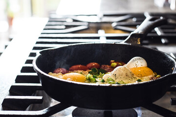 Breakfast eggs with tomatoes and green onions frying in cast iron pan