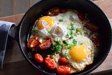 Top down view of breakfast eggs with tomatoes and green onions in cast iron pan