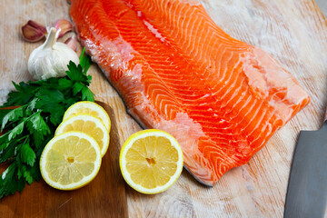 Fresh salmon fillet on wooden surface with lemon and greens prepared for cooking