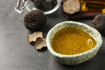 Fresh truffle oil in bowl on grey table, closeup. Space for text