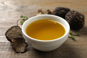 Fresh truffle oil in bowl on wooden table, closeup