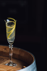 champagne flute with long lemon zest on wooden barrel with dark background