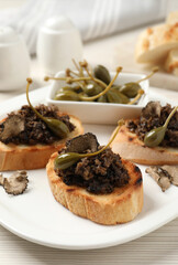 Delicious bruschettas with truffle sauce and caperberries on white wooden table, closeup