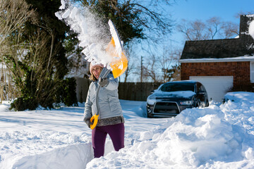 Woman shoveling snow out of driveway with car and home in background. Movement and action.