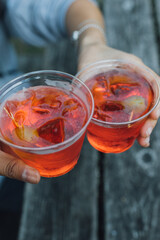 cheers with two aperol spritz cocktails in plastic cups