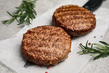 Tasty grilled hamburger patties, knife and seasonings on grey table, closeup