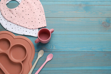 Flat lay composition with drool baby bibs and plastic dishware on light blue wooden background....