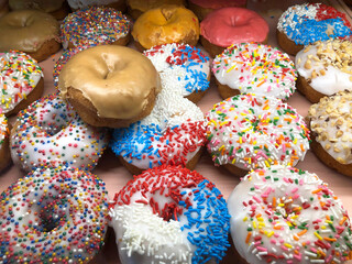 Vanilla frosted donuts with candy sprinkles on display for sale. High sugar fast food treat