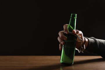 Alcohol addiction. Man handcuffed to bottle of beer at wooden table, closeup. Space for text
