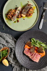 Set  from fish on plate. Risotto with slice roasted white fish, tuna steak with tomato salsa and nori. Trendy composition on dark background. Minimal composition from fish on black table with textile.