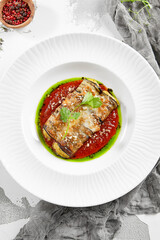 Eggplant rolls stuffed with tomato and cheese. Baked eggplant and cheese rollatini. Eggplant appetizer in white plate on stone background. Plant-based menu.