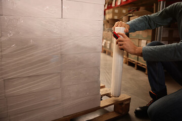 Worker wrapping boxes in stretch film at warehouse, closeup