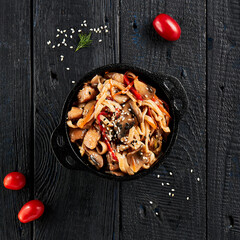 Stir fried udon noodles in wok. Udon noodle with chicken and mushrooms on wooden background. Asian...