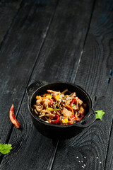 Yakisoba noodle with chicken and vegetables on wooden background. Japanese stir fry noodles in wok on black table with ingredients. Chicken with buckwheat soba on wok. Oriental cuisine. Wok menu.