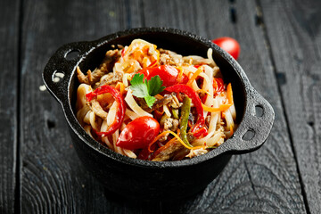Japanese stir fryed udon noodles in wok. Udon noodle with beef and vegetables on wooden background. Asian noodles on black table with ingredients. Wok menu.