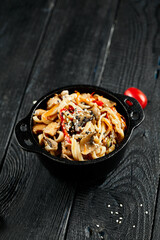 Stir fried udon noodles in wok. Udon noodle with chicken and mushrooms on wooden background. Asian noodles on black table with ingredients. Wok menu for japanese restaurant.