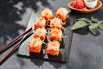 Maki sushi on dark stone table. California maki with tobiko. Sushi roll with fish inside, maguro and cheese outside. Style concept japanese menu with black background, leaves and hard shadow.