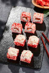 Maki sushi on dark slate.  Maki roll with crab topped. Sushi roll with crab, cream chees and tobika. Style concept japanese menu with black background, leaves and hard shadow.