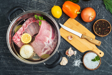 pot of water and meat prepared for boiling. seasonings and vegetables on a black table.
