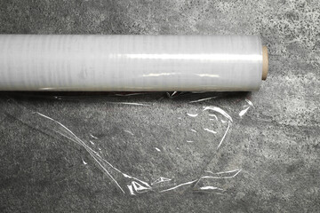 Roll of transparent plastic stretch wrap on grey table, closeup