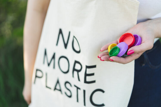 Woman hands are holding a handful of multi-colored plastic lids. Concept of environmental pollution, eco friendly behavior, waste sorting and plastic recycling.