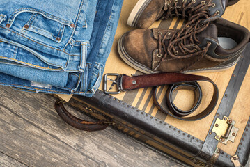 worn boots, a belt and a stack of blue jeans lie on a vintage suitcase. The concept of travel and comfortable equipment.