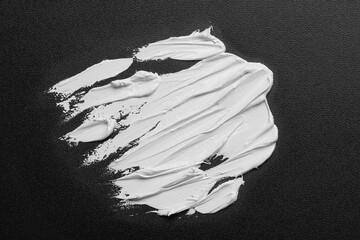 Strokes of white oil paint on black canvas, top view