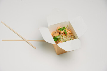 Asian food in the box with wooden sticks on white background. Salad. Greenery. Seafood. Minimalist. Advertisement. Food delivery. East culture. Asian kitchen.