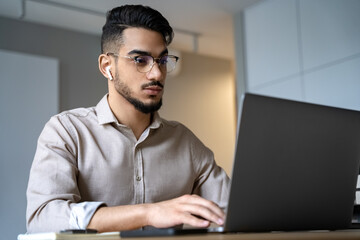 Portrait of young indian man looking at laptop screen sitting at home office