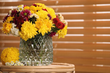 Bouquet of beautiful chrysanthemum flowers on wicker table near window indoors, space for text