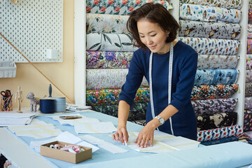 Asian woman seamstress drawing pattern on fabric for dress tailoring.