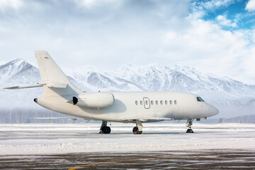 Fototapeta na wymiar White luxury executive business jet on the winter airport apron on the background of high scenic mountains