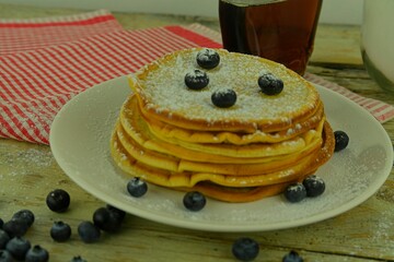 Delicious pancakes with fresh blueberries and syrup on a rustic wooden table. Maple syrup and the blueberries on stack of pancakes. Rustic white table. Close-up