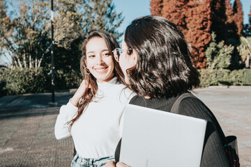 Two friends studying together at university campus walking going to class while smiling and chit...