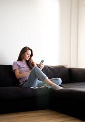 A young woman is sitting on a sofa and using her phone