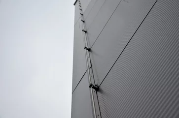 Foto op Canvas The lightning conductor is used to protect buildings from lightning, which can damage the house or industrial hall. grounding wire routing along a gray metal sheet facade. plastic holders © Michal