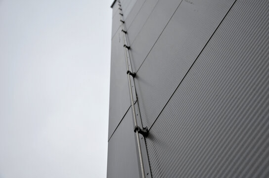 The lightning conductor is used to protect buildings from lightning, which can damage the house or industrial hall. grounding wire routing along a gray metal sheet facade. plastic holders