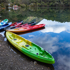 Colorful boats on the shore of a lake with the reflection of sky and hills 