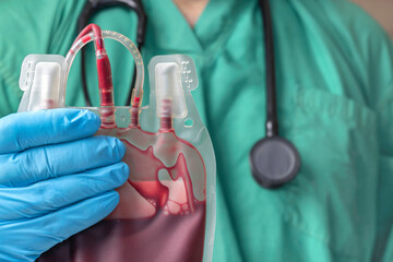 A doctor in green surgical shirt and blue glove holding a blood bag.    Blood transfusion and blood...