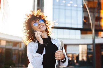 Businesswoman with curly hair wearing eyeglasses and casual clothes walking on city street and...