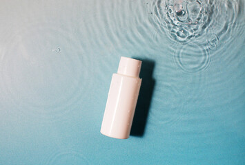  White cosmetic bottle in a blue pool with water and waves. Spa skin care.
