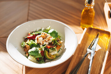 Salad of fresh vegetables with strachatella and pine nuts on the table in restaurant on hard sunlight