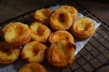 pile of egg tarts in a wire cooling rack against dark background  