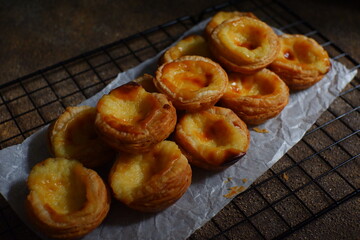pile of egg tarts in a wire cooling rack against dark background  