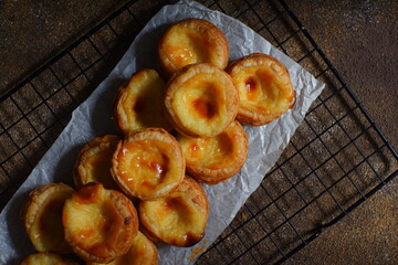 pile of egg tarts in a wire cooling rack against dark background  