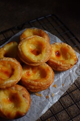 pile of egg tarts in a wire cooling rack against dark background  