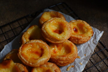 pile of egg tarts in a wire cooling rack against dark background  
